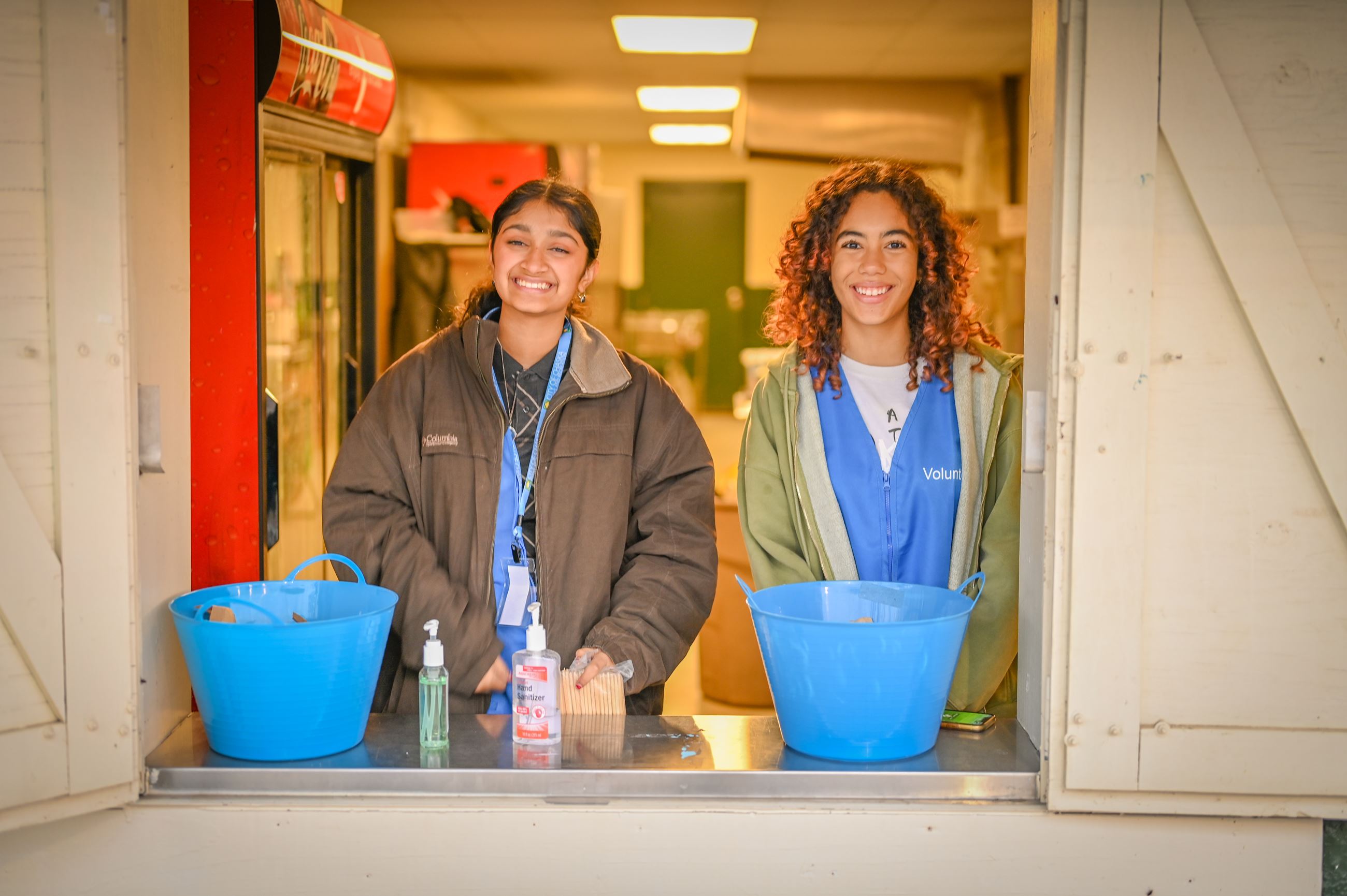 Two young women wearing blue vests, smiling at camera, inside concessions stand